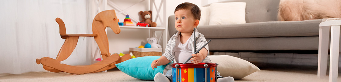 foto de bebé sentado en el piso jugando con un tambor para niños, en un cuarto donde abundan juguetes.