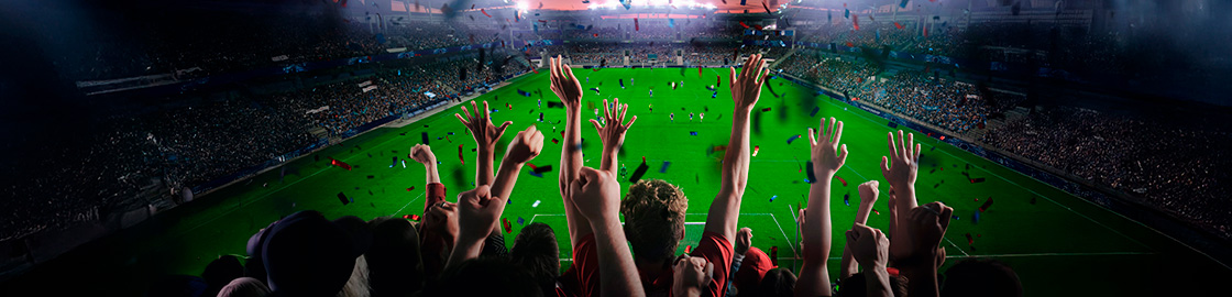 foto de un estadio de fútbol, donde muchos aficionados celebran desde la tribuna con los brazos levantados.