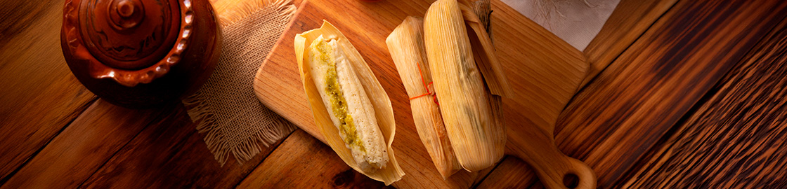 foto de tamales sobre una mesa de madera, donde uno tiene la hoja abierta y está cortado por la mitad.