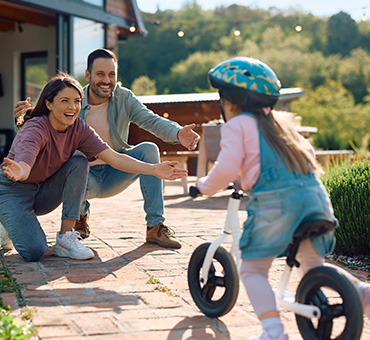foto de niña aprendiendo a andar en bicicleta, rodando hacia sus padres que la reciben emocionados.