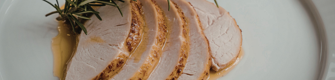 Foto de un plato con rodajas de pavo bañadas en salsa, acompañadas de un romero decorativo.