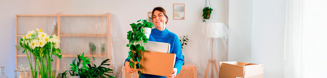 Foto de mujer joven sonriente cargando cajas durante una mudanza.