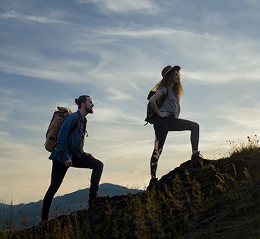 Foto de un hombre y una mujer practicando senderismo, subiendo una colina al atardecer. 