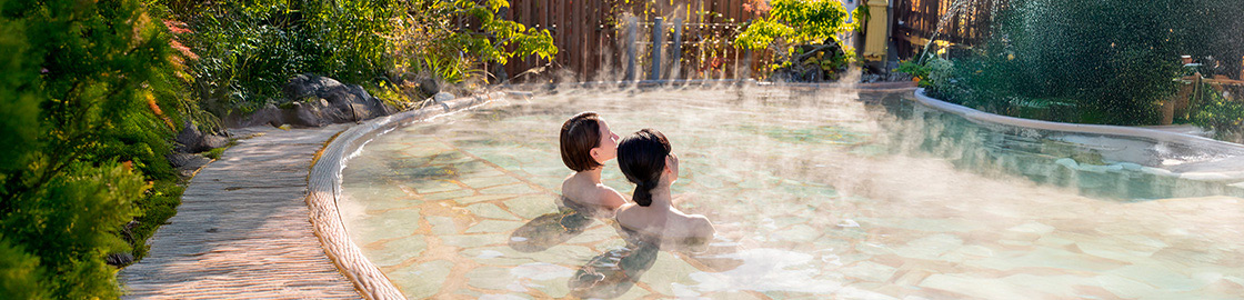 Foto de dos mujeres de espaldas, dándose un baño en aguas termales rodeadas de naturaleza.