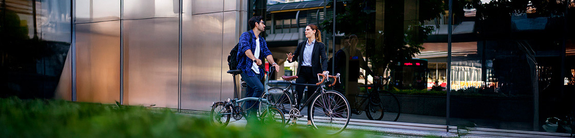Foto de un hombre y una mujer, cada uno con su bicicleta, conversando frente a un edificio.