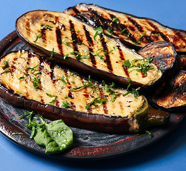 Foto de un plato de rodajas de berenjena a la parrilla sobre un fondo azul.