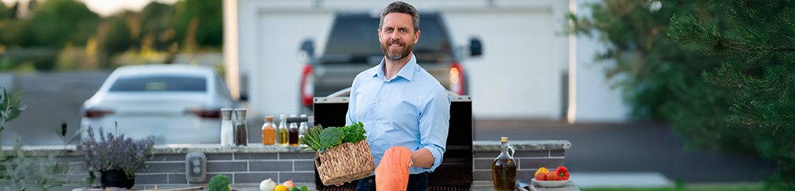 Foto de un hombre de mediana edad en el patio de su casa sosteniendo un pescado de salmón frente al asador.