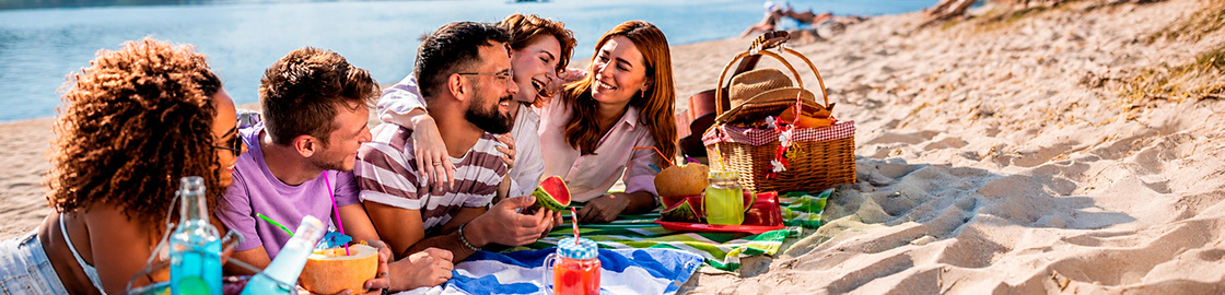 Foto de un grupo de amigos haciendo picnic en la playa, comiendo frutas.