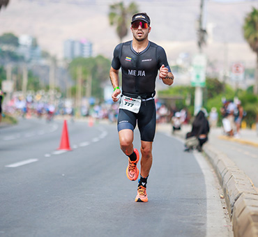 Foto de un hombre con ropa deportiva y su número de participante corriendo durante un triatlón