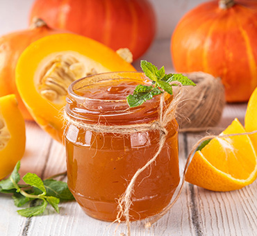 Foto de un frasco con mermelada de calabaza sobre una mesa de madera, con naranjas y calabazas a su alrededor